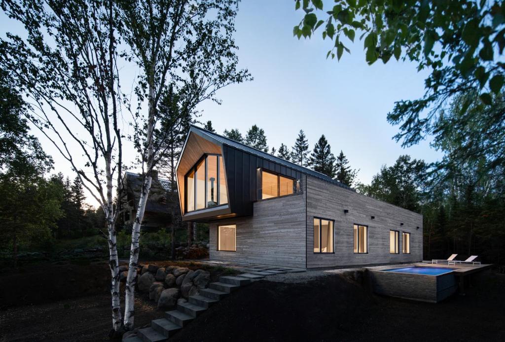 a modern house with a swimming pool and a tree at Luxurious Chalet with Pool, Sauna, Spa & Amazing View in La Malbaie