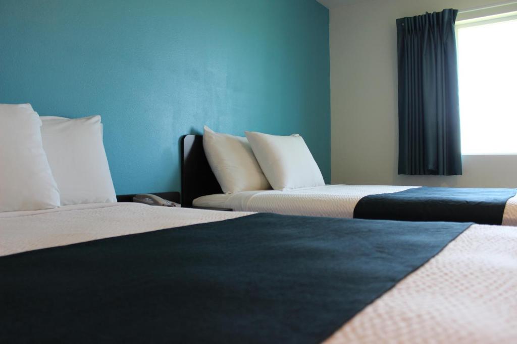 2 camas en una habitación con paredes azules y ventana en Motel 6 Rexburg, ID en Rexburg