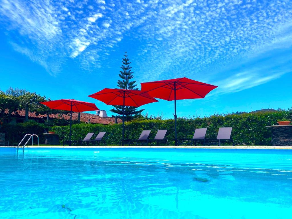 una piscina con sombrillas y sillas rojas en Quinta Dom Sapo - Agroturismo en Viana do Castelo