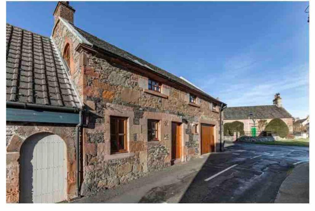 an old brick building with a white door on a street at The Stables, charming converted, 2 bedroom Cottage, Melrose in Darnick