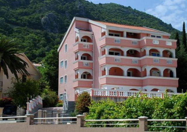 a pink building with a palm tree in front of it at Vila Tamara Apartmani in Bečići