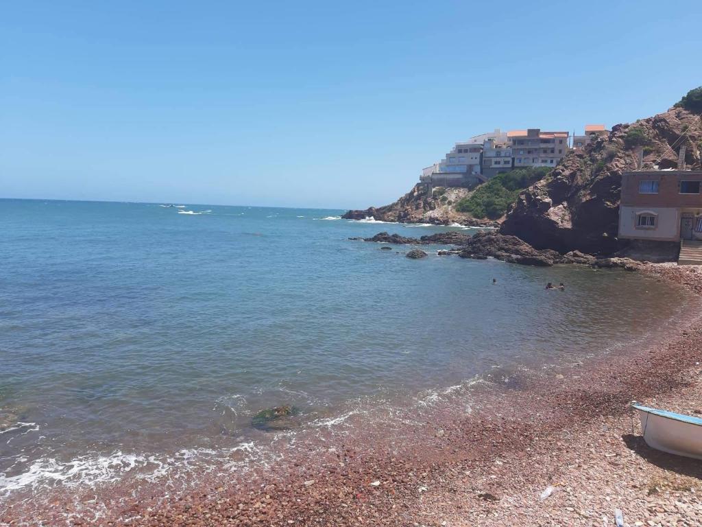 una playa rocosa con un barco en la orilla en Suite home beldj en Tipaza