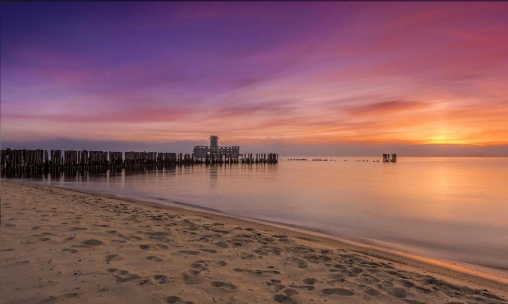 a beach with a pier in the water at sunset at Apartament Nadia in Gdynia