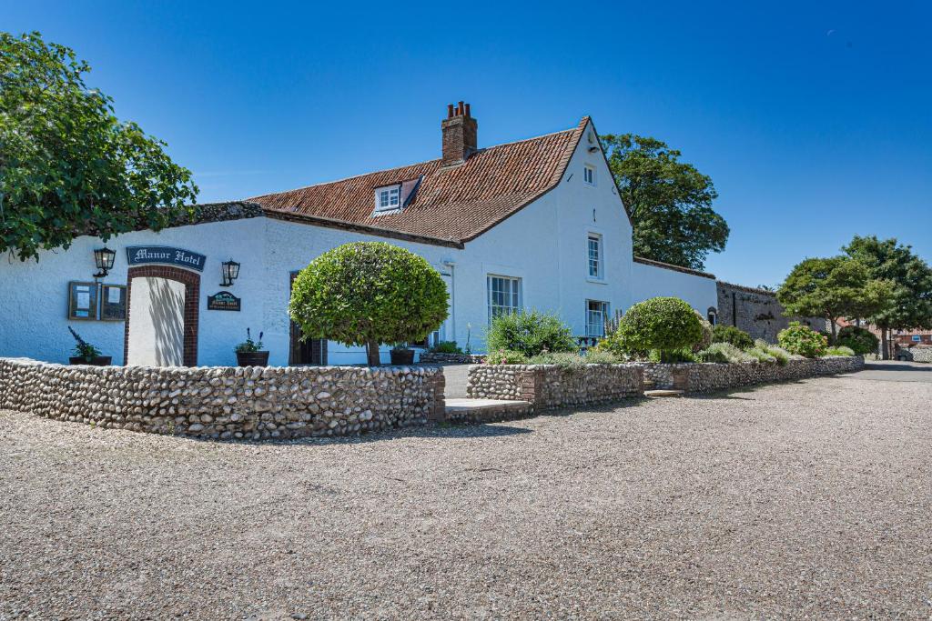 a white house with a stone wall in front of it at The Manor Coastal Hotel & Inn, Blakeney - part of The Coaching Inn Group in Blakeney