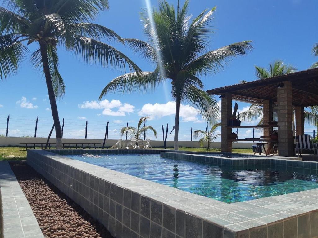 a swimming pool with palm trees and a gazebo at Morada da Praia - Porto de Pedras à Beira-Mar in Pôrto de Pedras