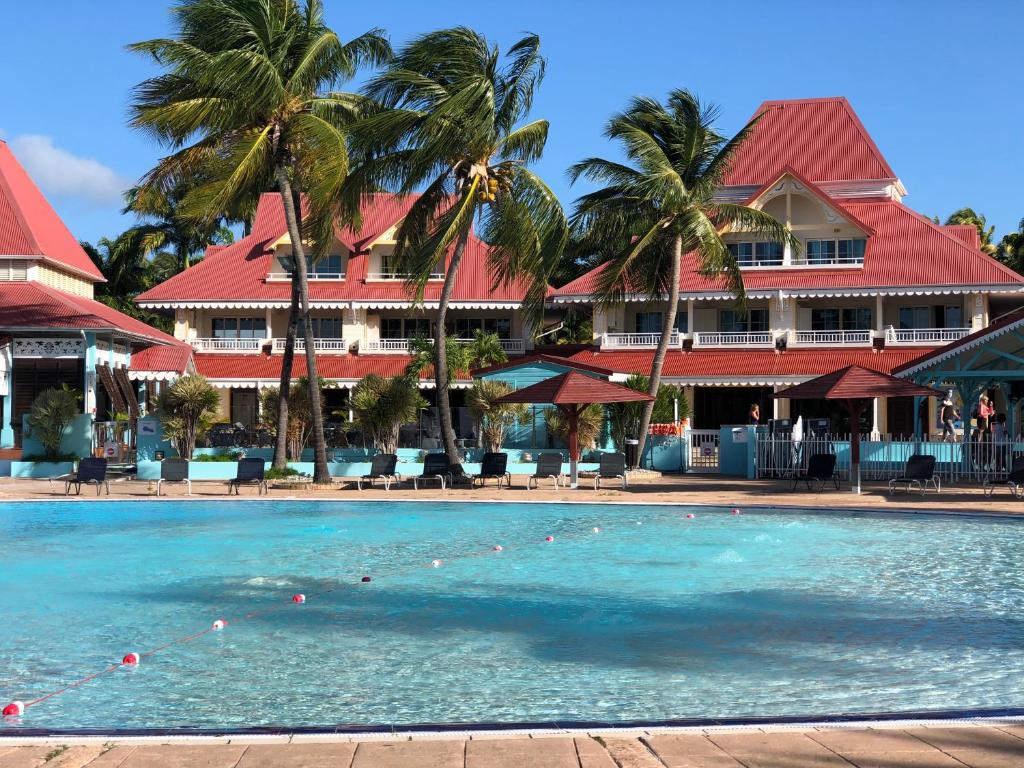 a swimming pool in front of a hotel with palm trees at Suite 4 pers dans village vacances in Sainte-Anne