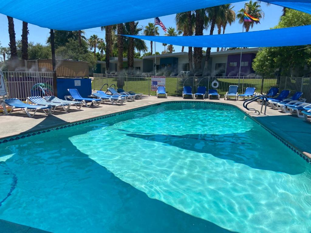 uma piscina com cadeiras e um guarda-sol azul em CCBC Resort Hotel - A Gay Men's Resort em Cathedral City