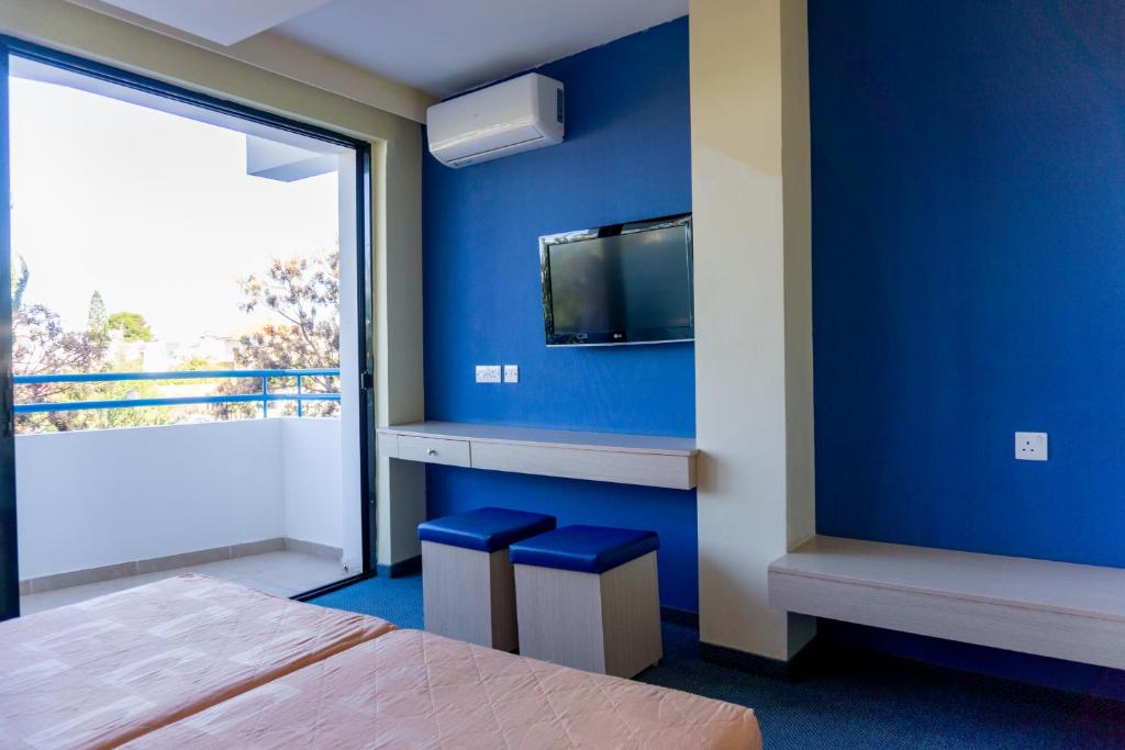 een slaapkamer met een blauwe muur met een tv en krukken bij Mariandy Hotel in Larnaka