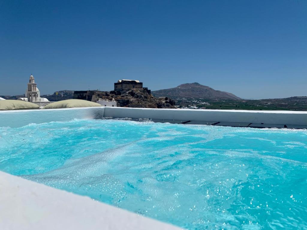 a large pool of blue water with a city in the background at White Curves Santorini in Akrotiri