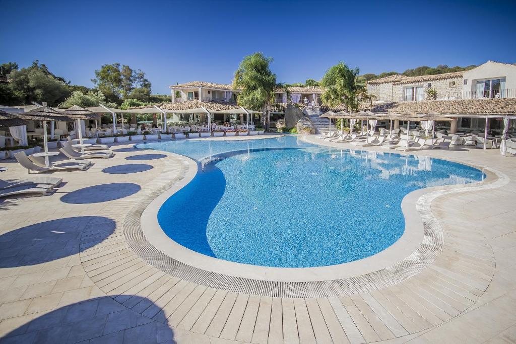 una grande piscina con sedie e ombrelloni di Villas Resort Wellness & SPA a Castiadas