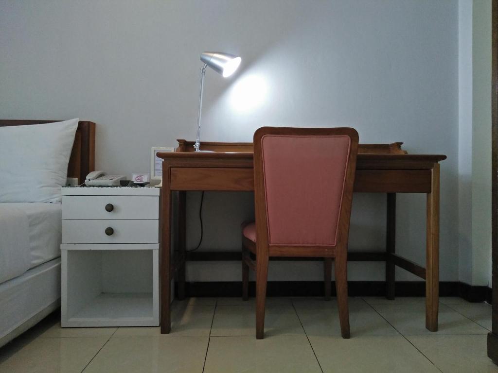 A compact wooden desk beside the bed provides a single chair and desk lamp.