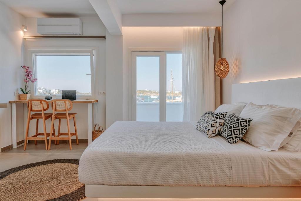 a white bedroom with a bed and a desk and windows at Nautica Suites - Modern Seaview Suite in Antiparos Town