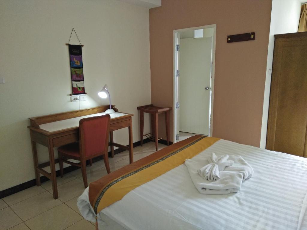 A bedroom with a work desk, chair, stool, wardrobe, and towel-decorated bed.