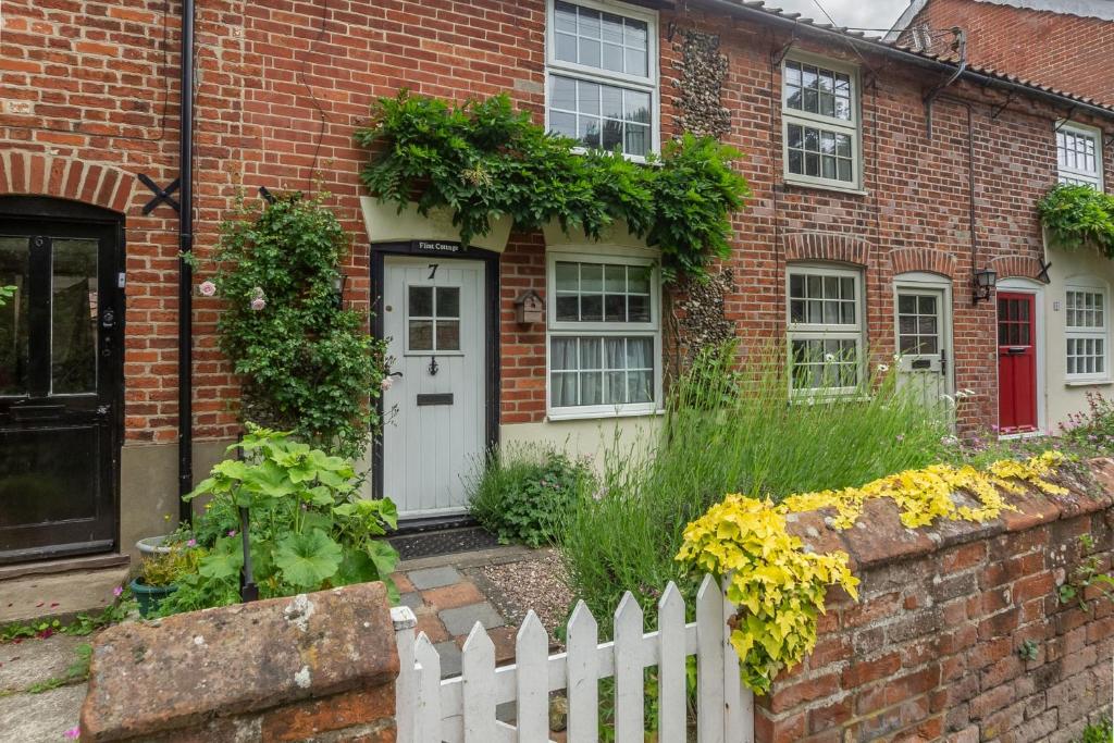 a brick house with a white fence and flowers at Flint Cottage in Wenhaston