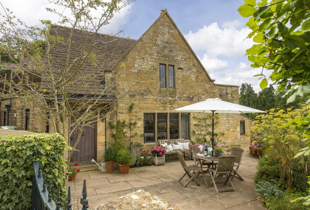 a stone house with a patio with a table and an umbrella at Apple Cottage in Snowshill
