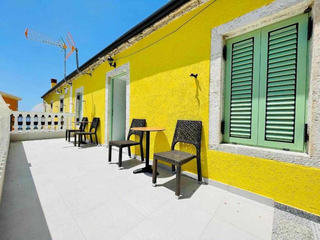 a yellow wall with chairs and tables on a patio at Mpolanos Guesthouse in Himare