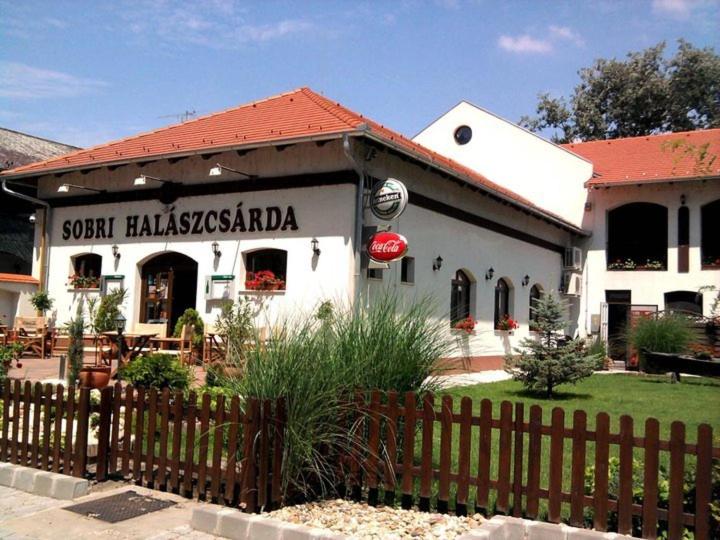un restaurant avec une clôture en face d'un bâtiment dans l'établissement Sobri Halászcsárda és Panzió, à Baja