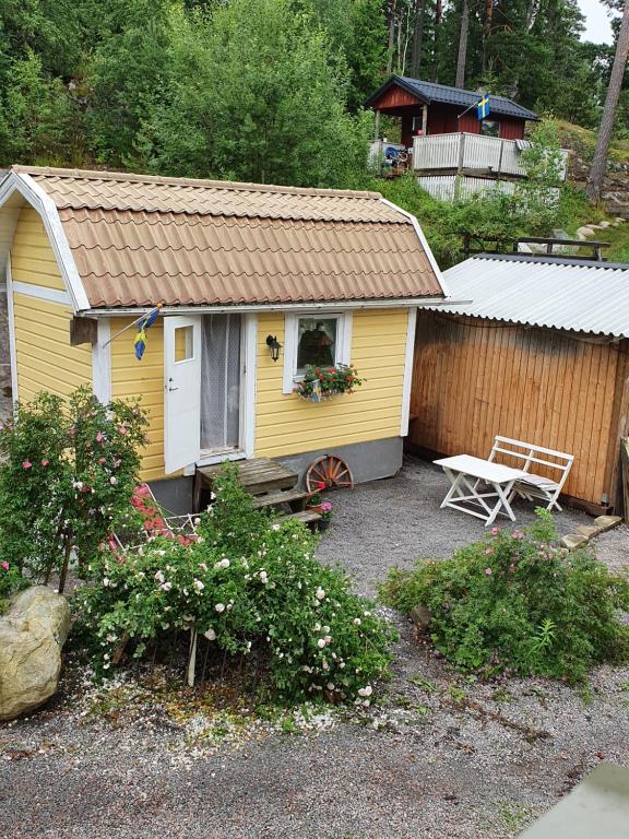 a small yellow house with a bench and a fence at Sjönära liten stuga med sovloft, toilet in other small house, no shower in Åkersberga