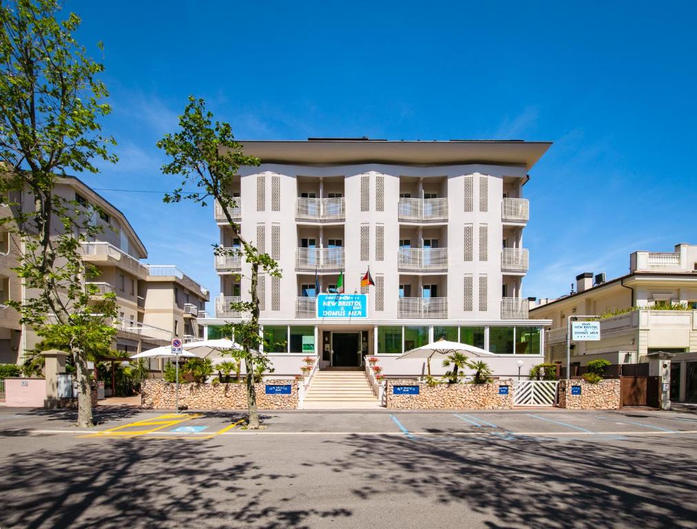 een groot wit gebouw met parasols ervoor bij New Bristol Sport Hotel in Cesenatico