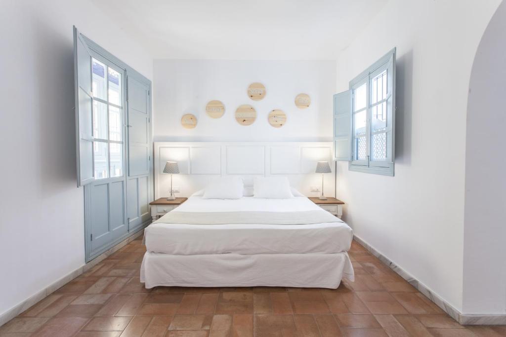a white bedroom with two beds and two windows at Apartamentos Suites Santa Cruz in Seville