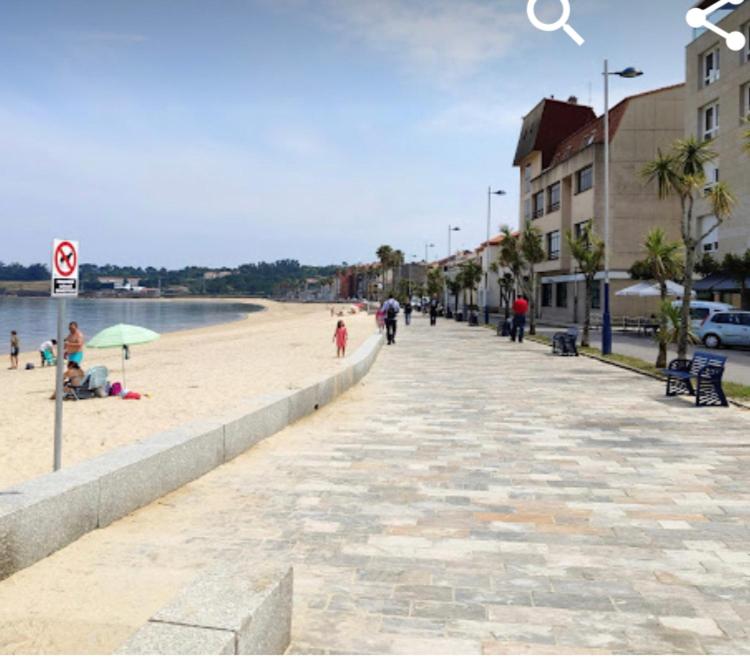 einen Strand mit Leuten, die auf dem Sand und in Gebäuden spazieren gehen in der Unterkunft Casa en la playa in Pobra do Caramiñal