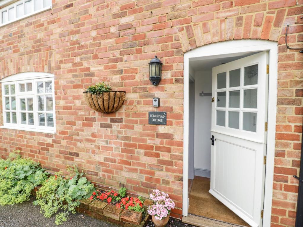 a brick house with a white door and flowers at Homestead Cottage in Shipston-on-Stour