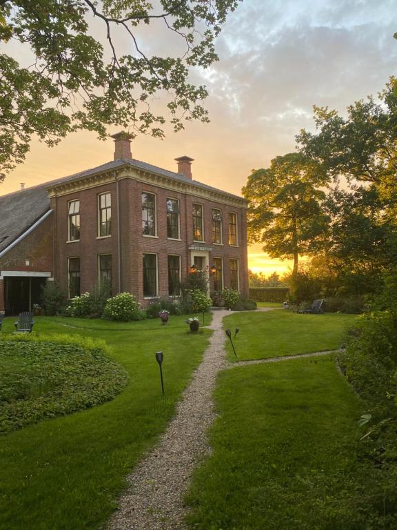 een groot bakstenen huis met een grindpad ervoor bij Bed and Breakfast Batenborg in Winsum