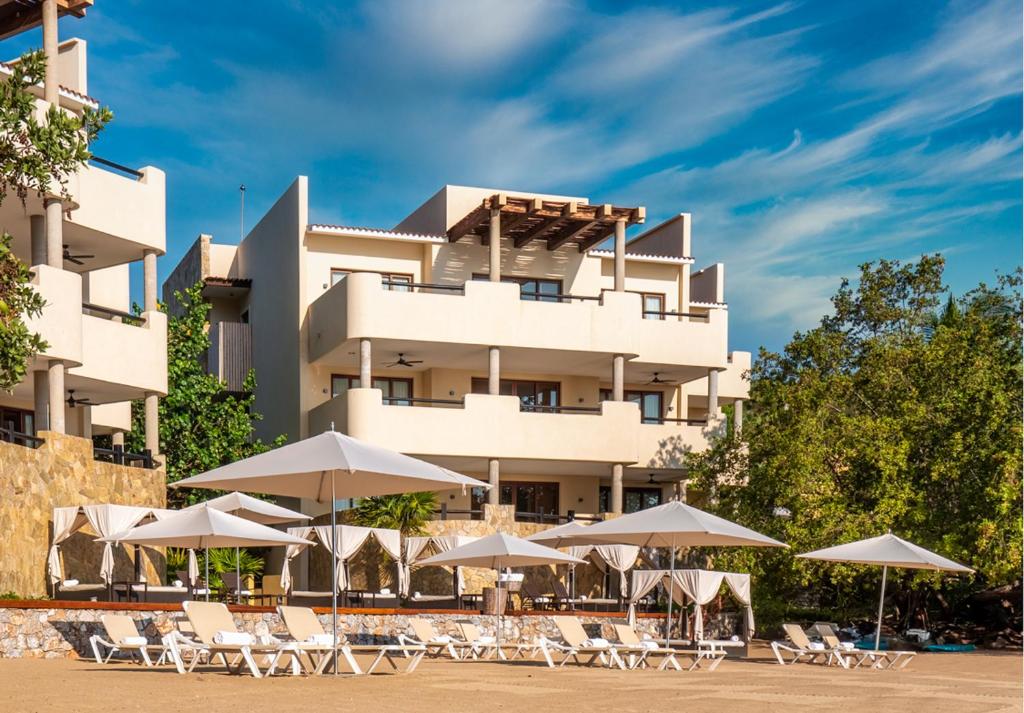 a hotel with chairs and umbrellas in front of it at Celeste Beach Residences Huatulco Curamoria Collection in Santa Cruz Huatulco