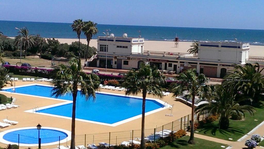 ein Resort mit zwei Pools und Palmen und dem Meer in der Unterkunft PRECIOSO APARTAMENTO EN PRIMERA LÍNEA DE PLAYA in Isla Canela