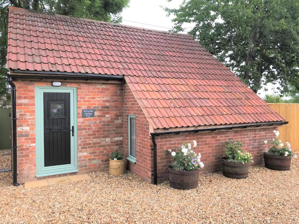 a brick shed with a red roof and three potted plants at The Lodge in North Bradley