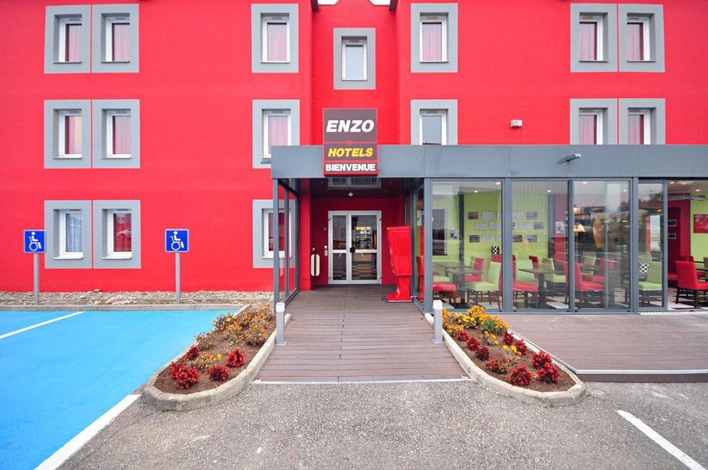 Enzo Hotel Mulhouse Sud Morschwiller By Kyriad Direct في Morschwiller-le-Bas: مبنى احمر وامامه زهور