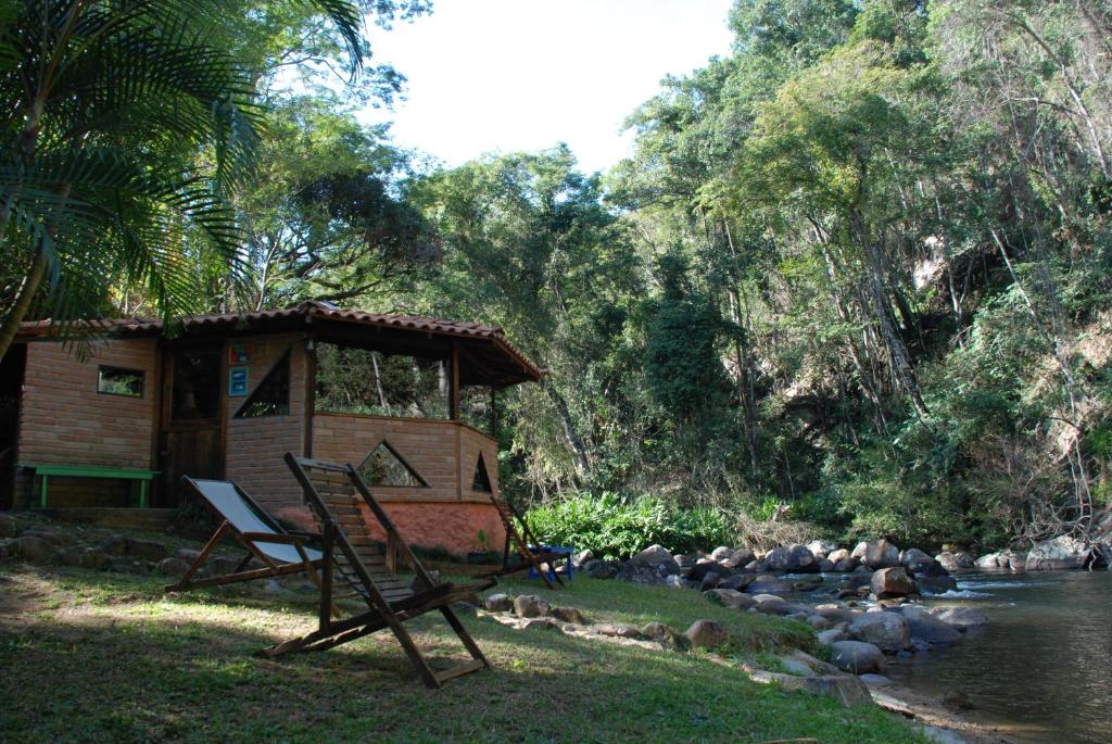 une cabane avec une chaise à côté d'une rivière dans l'établissement Pousada Estância Rio Acima, à Itamonte