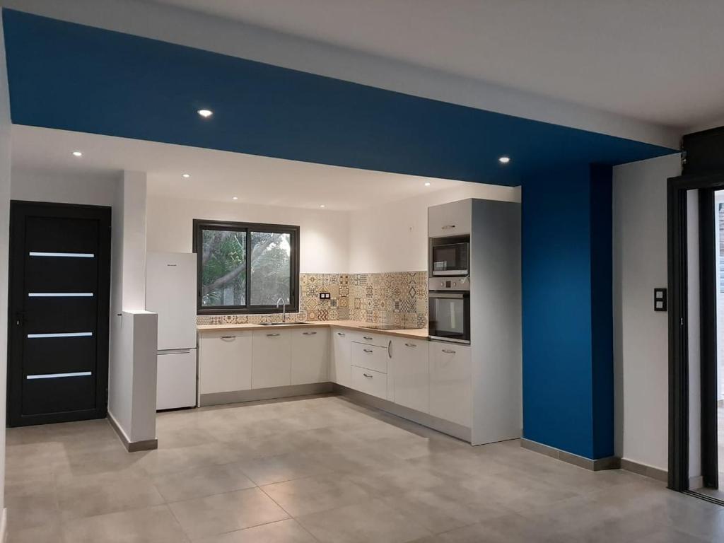 a large kitchen with white cabinets and a blue wall at La Caz' Miness in Saint-Louis