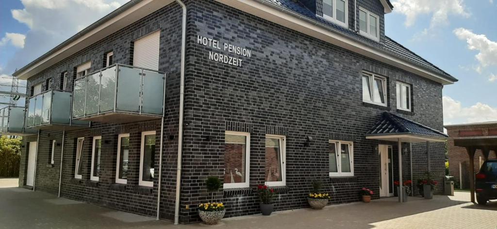 a black brick building with a balcony on it at Hotel Pension Nordzeit in Norddeich