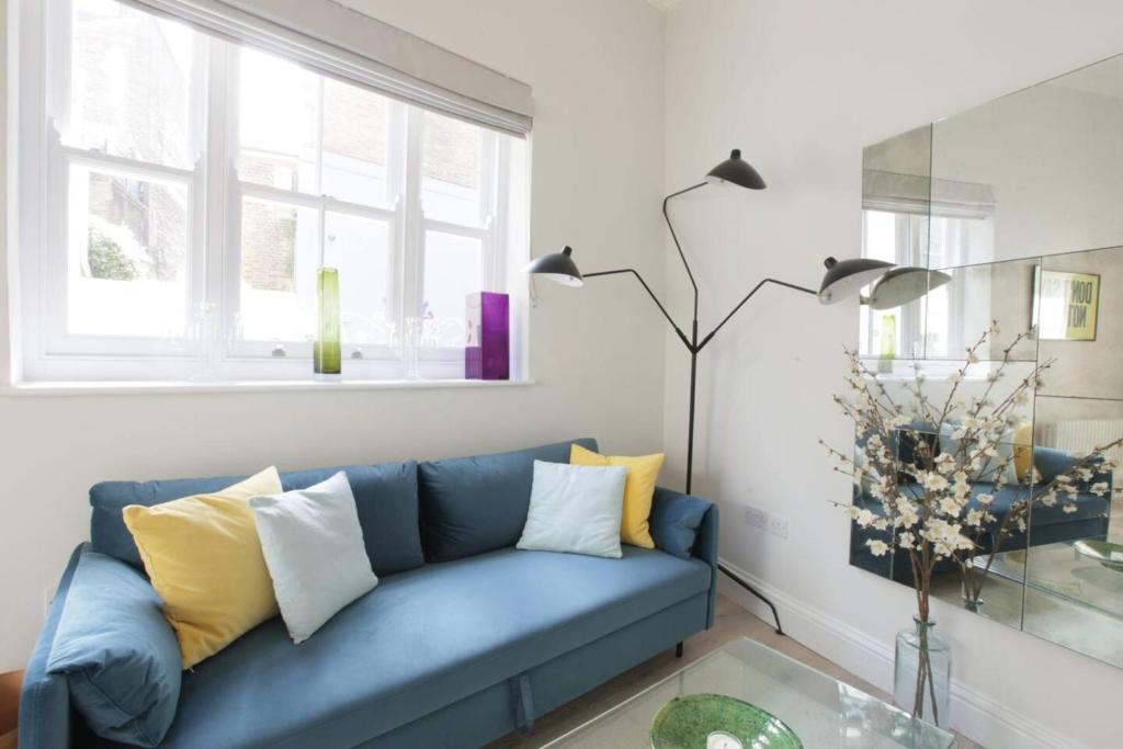 ein blaues Sofa im Wohnzimmer mit einem Glastisch in der Unterkunft Newly Refurbished 1 Bedroom in Vibrant Notting Hill in London