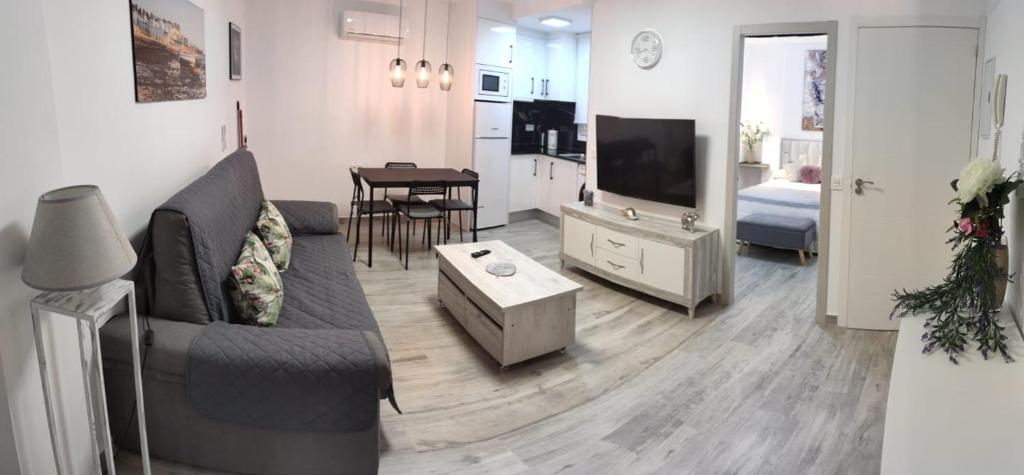 ein Wohnzimmer mit einem Sofa, einem TV und einem Tisch in der Unterkunft Apartamentos Sol y Luna Conil in Conil de la Frontera