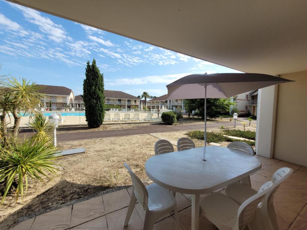 una mesa y sillas con una sombrilla en el patio en Appartement 6 places proche plage et avec piscine en Le Verdon-sur-Mer