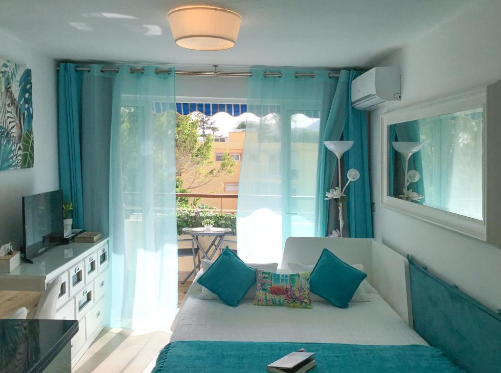 a living room with a bed with blue curtains and a television at Luminoso estudio a pie de playa in Estepona