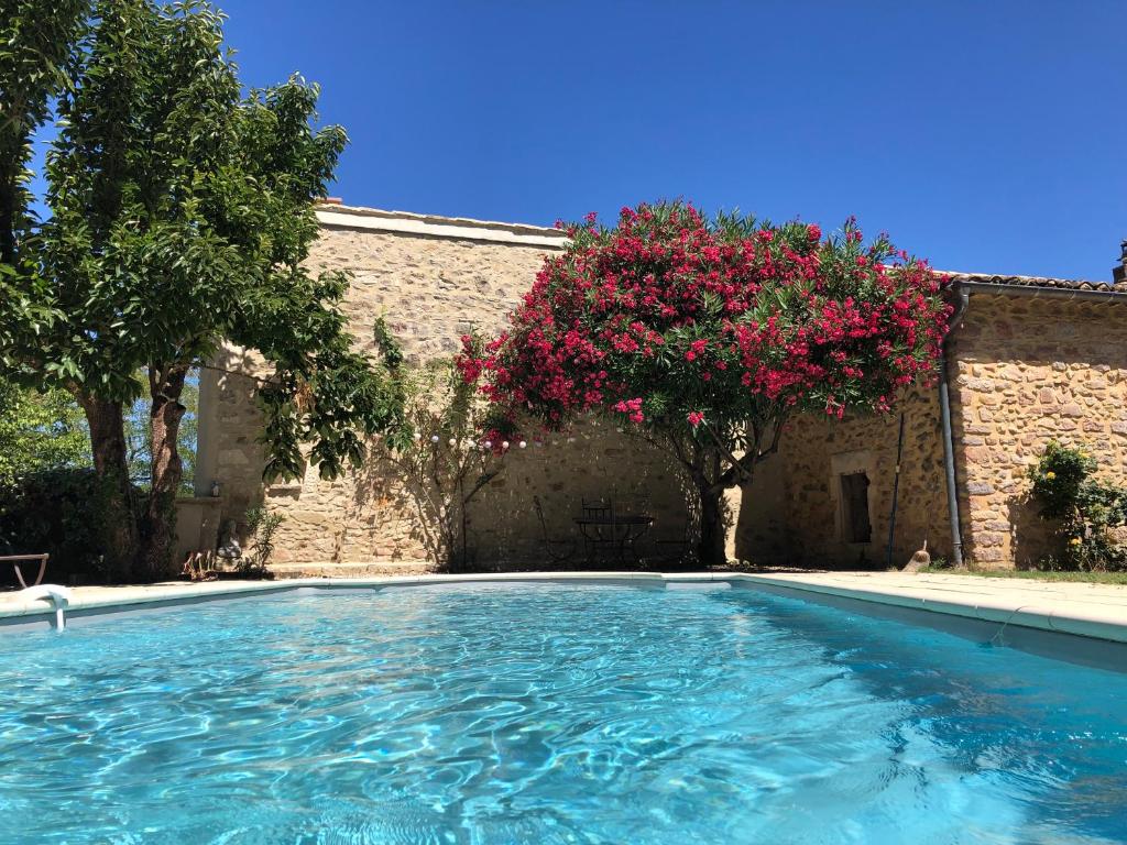 a swimming pool in front of a building with pink flowers at Maison des Bourgades in Saint-Julien-de-Peyrolas