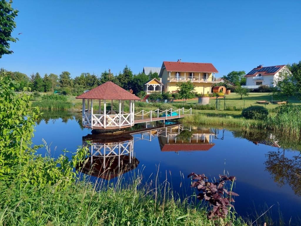 eine Brücke über einen Teich mit einem Haus im Hintergrund in der Unterkunft Dolina Miodu - Kaszuby, Sauna, Gorąca Balia in Borowina