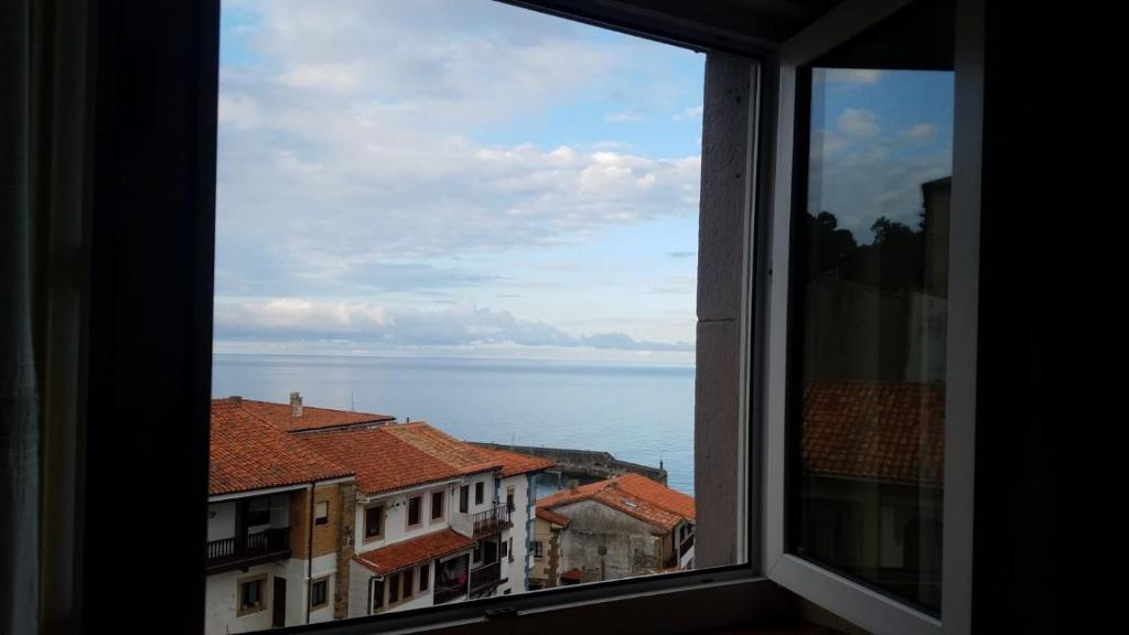a window with a view of the water and buildings at La casina del Reloj con vistas al mar in Lastres