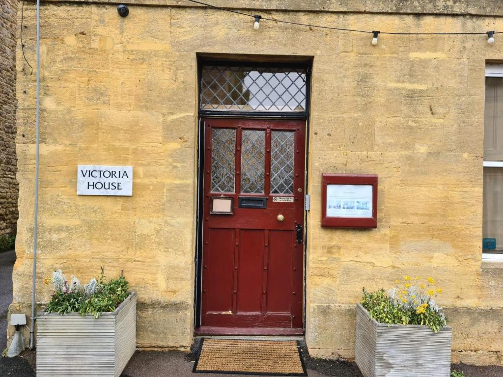 a red door on the side of a building with two plants at Victoria House in Stow on the Wold