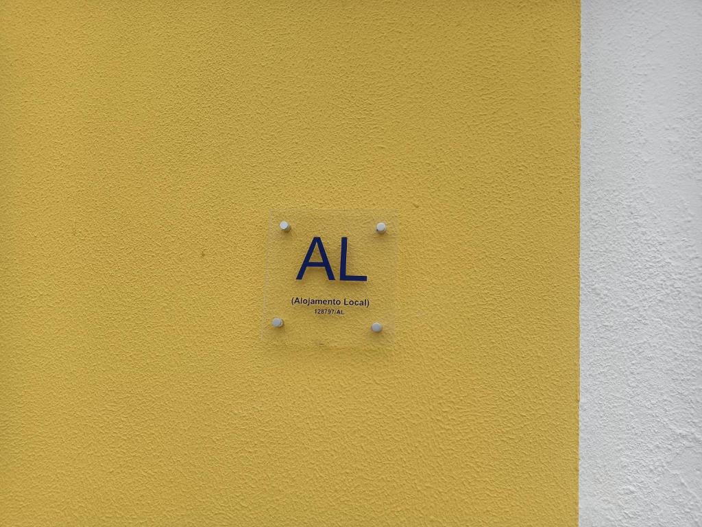 a sign on a yellow wall with the letters al at Alojamento Local Largo da Igreja in Santiago do Cacém