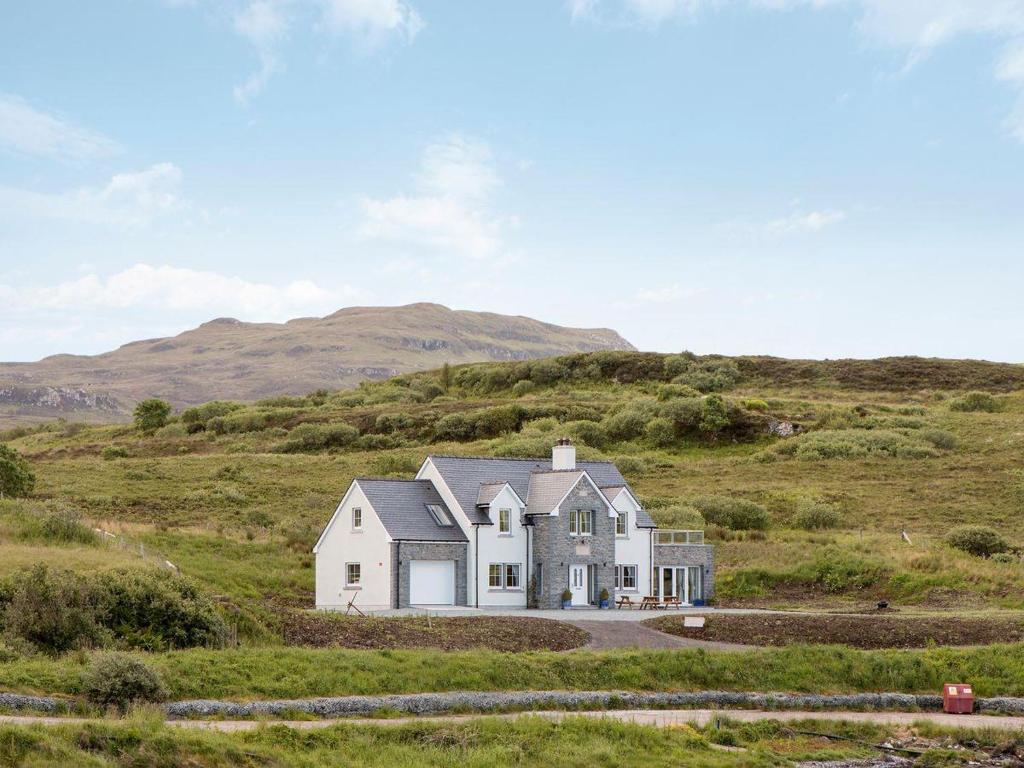 a house in a field with a hill in the background at Bracadale House in Port na Long