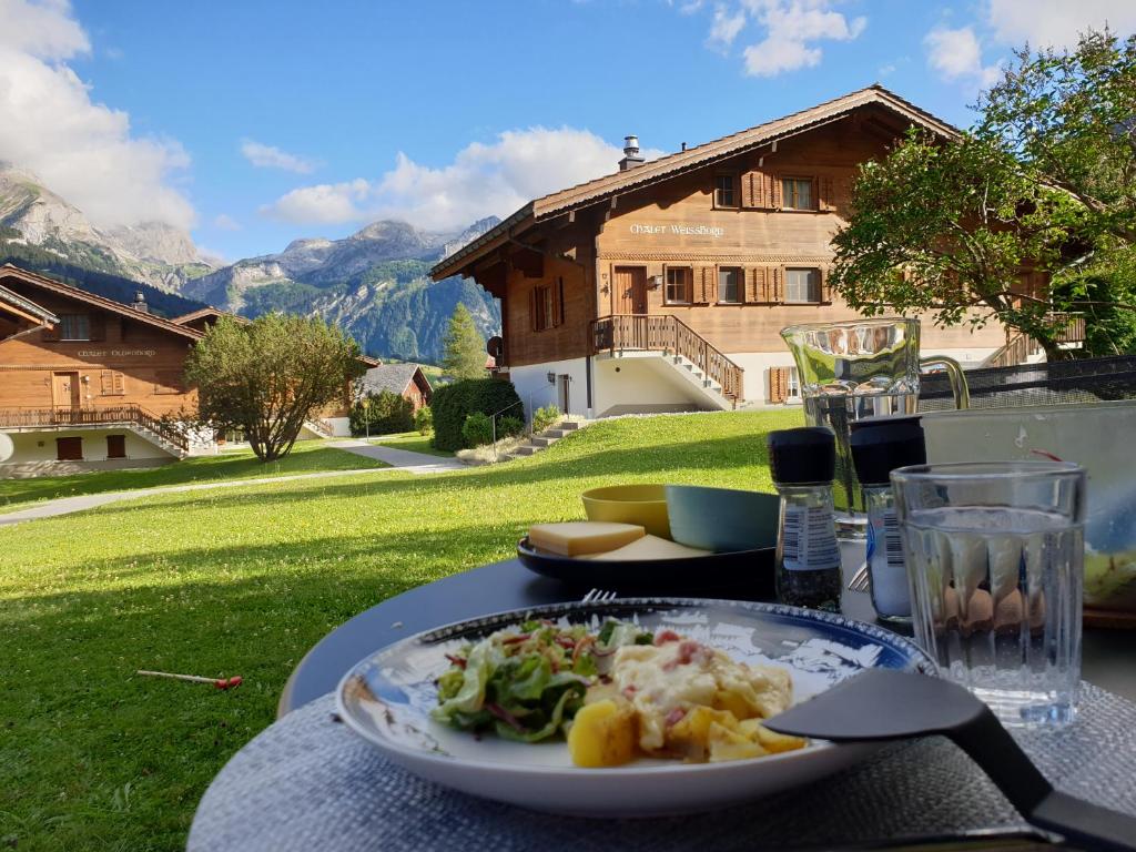 - une table avec une assiette de nourriture et une maison dans l'établissement Chalet Spitzhorn - Your Peak Getaway - Private Terrasse & gratis Parkplatz, à Gsteig