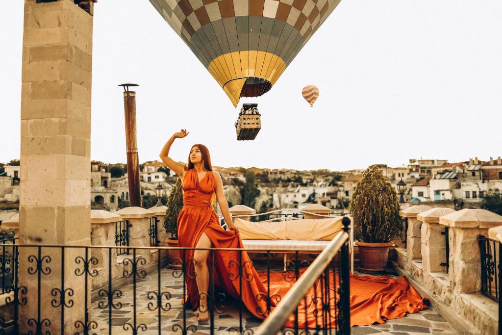 Castle Inn Cappadocia في أوروغوب: امرأة ترتدي ثوب برتقال تقف على شرفة مع بالون الهواء الساخن