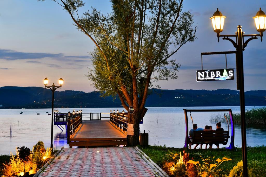 Nibras Villa Resort Hotel في صبنجة: أناس يجلسون على مقعد على رصيف الميناء بالقرب من البحيرة