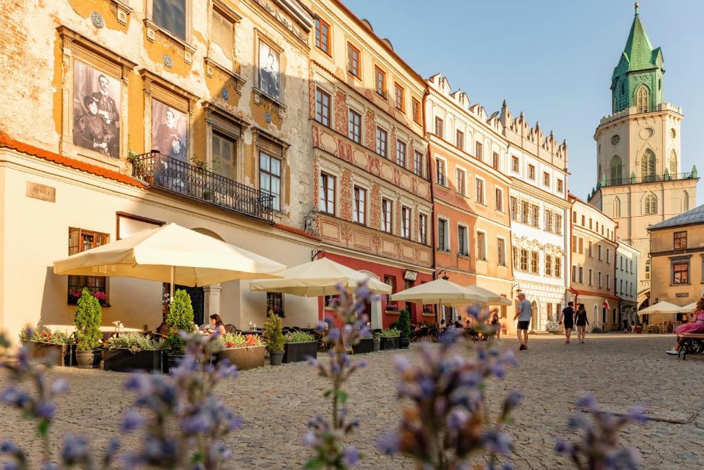 een stadsstraat met tafels, parasols en gebouwen bij Rynek 10 Apartments in Lublin