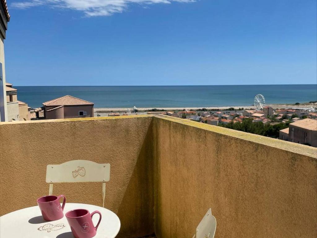 - une table et deux tasses sur un balcon avec vue sur l'océan dans l'établissement Appt T2 avec piscine, tennis, parking privé, animaux admis - St Pierre la Mer - FR-1-229D-109, à Fleury