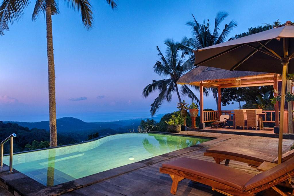 a swimming pool with two chairs and an umbrella at Loids Villa Eco Lodge Lempuyang in Seraya